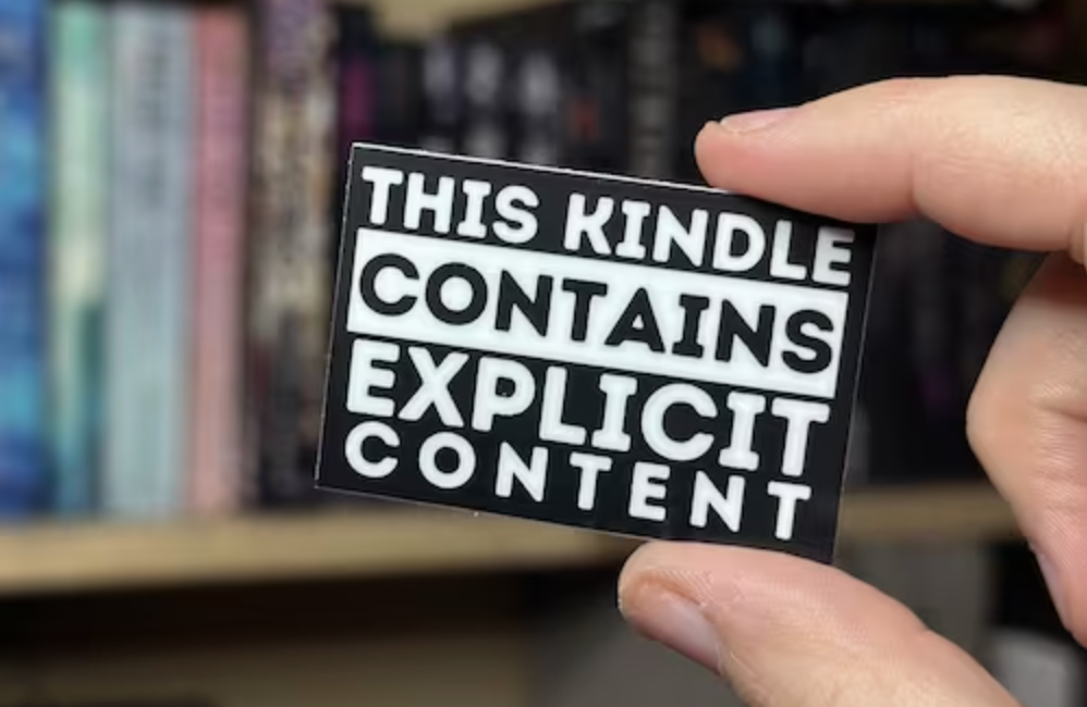 Hand holding a small sign that reads "This kindle contains explicit content"